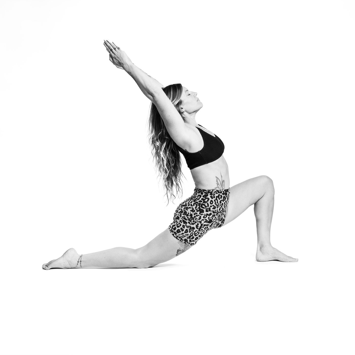 A teacher in a low lunge on white, arms reaching back overhead, eyes closed.