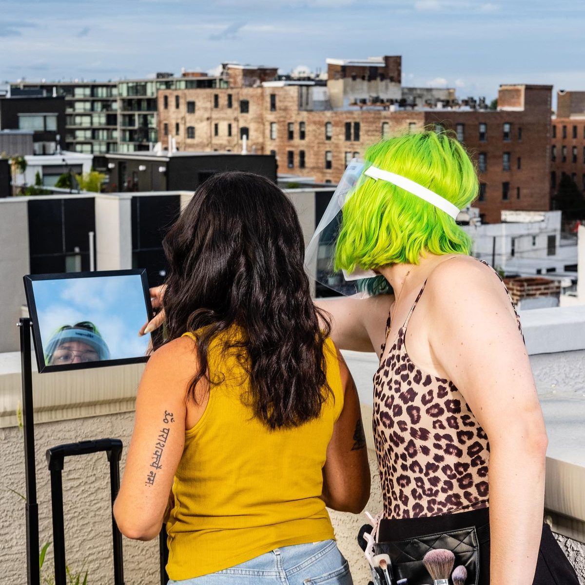 Two people standing at a tethered monitor between takes, city rooftops behind them.