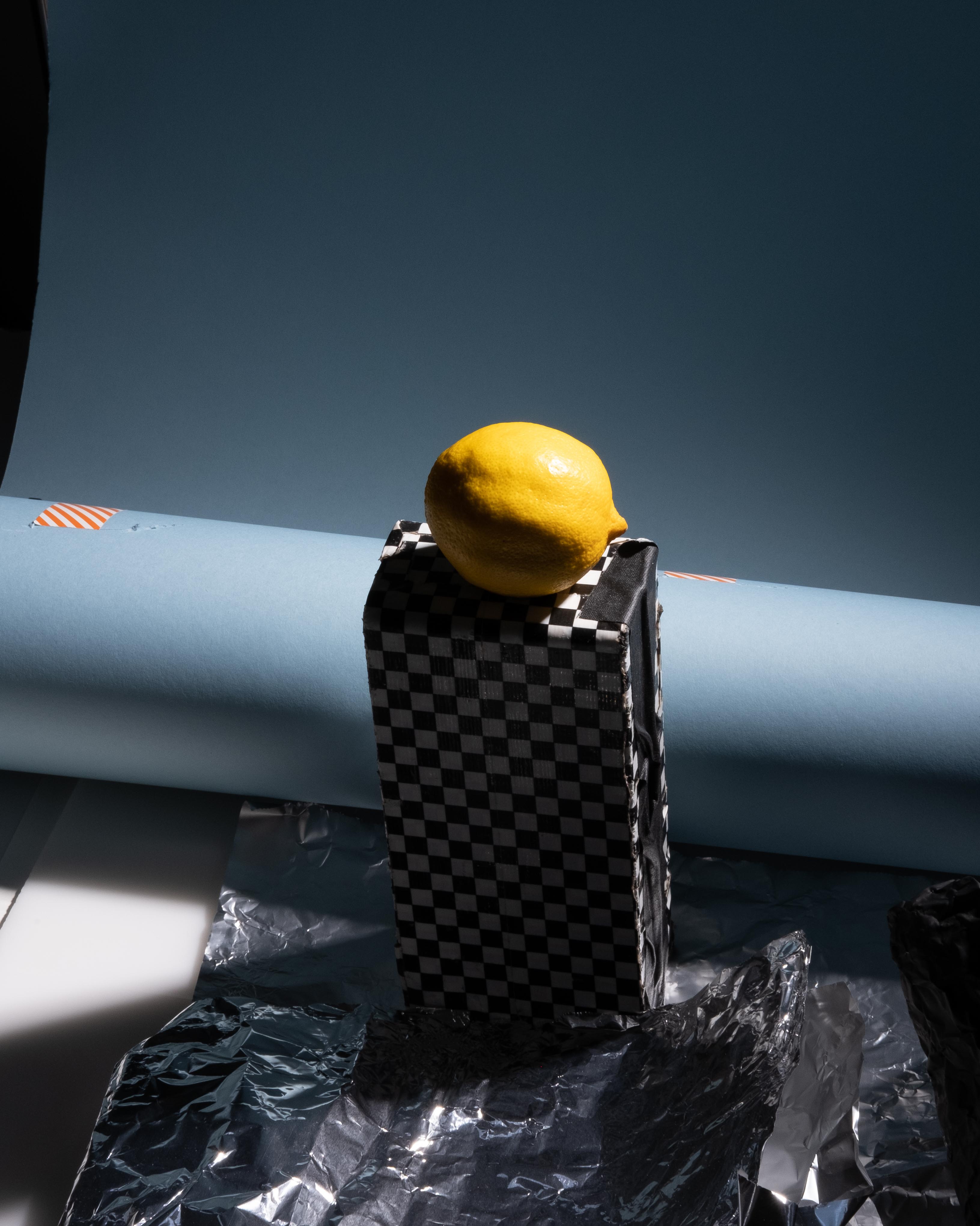 A lemon resting on a black-and-white checkered pedestal in a studio still life.